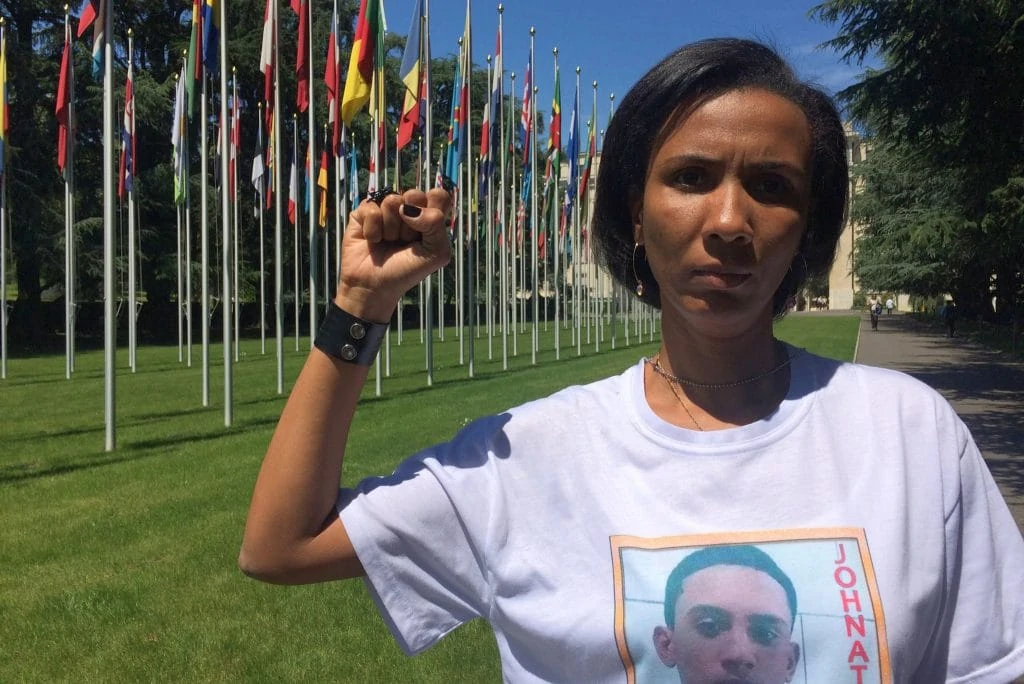 Ana Paula Gomes de Oliveira mit ihrer erhobenen Faust vor dem Gebäude der UNO. Hinter iher die Fahnen der Mitgliederländer.