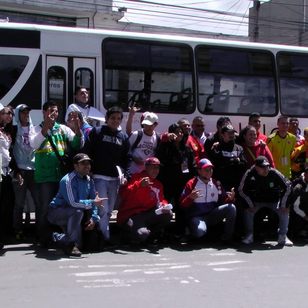 25 young people from 18 fan clubs and the FJMBN stand together in front of a white bus for a group photo.