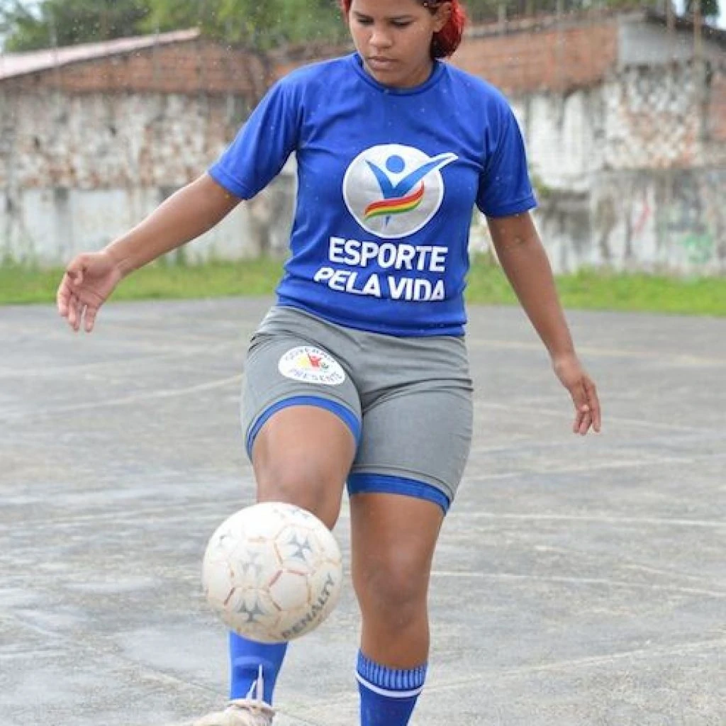 A teenager juggles a white football with her foot.