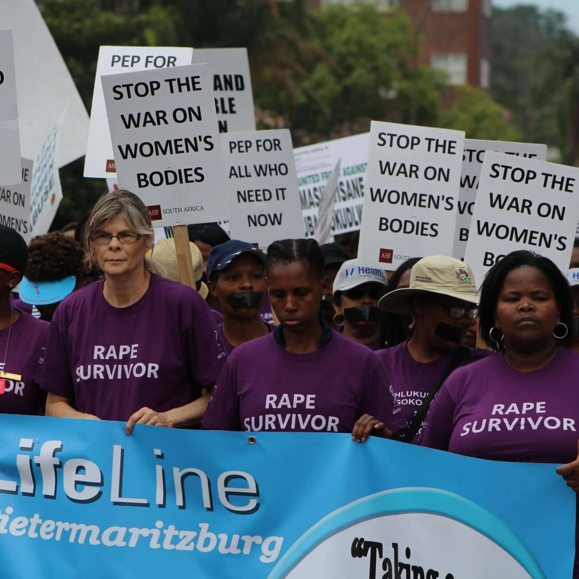 Women in purple T-shirts hold up white signs. In front of them a banner with the crawl Lifeline.