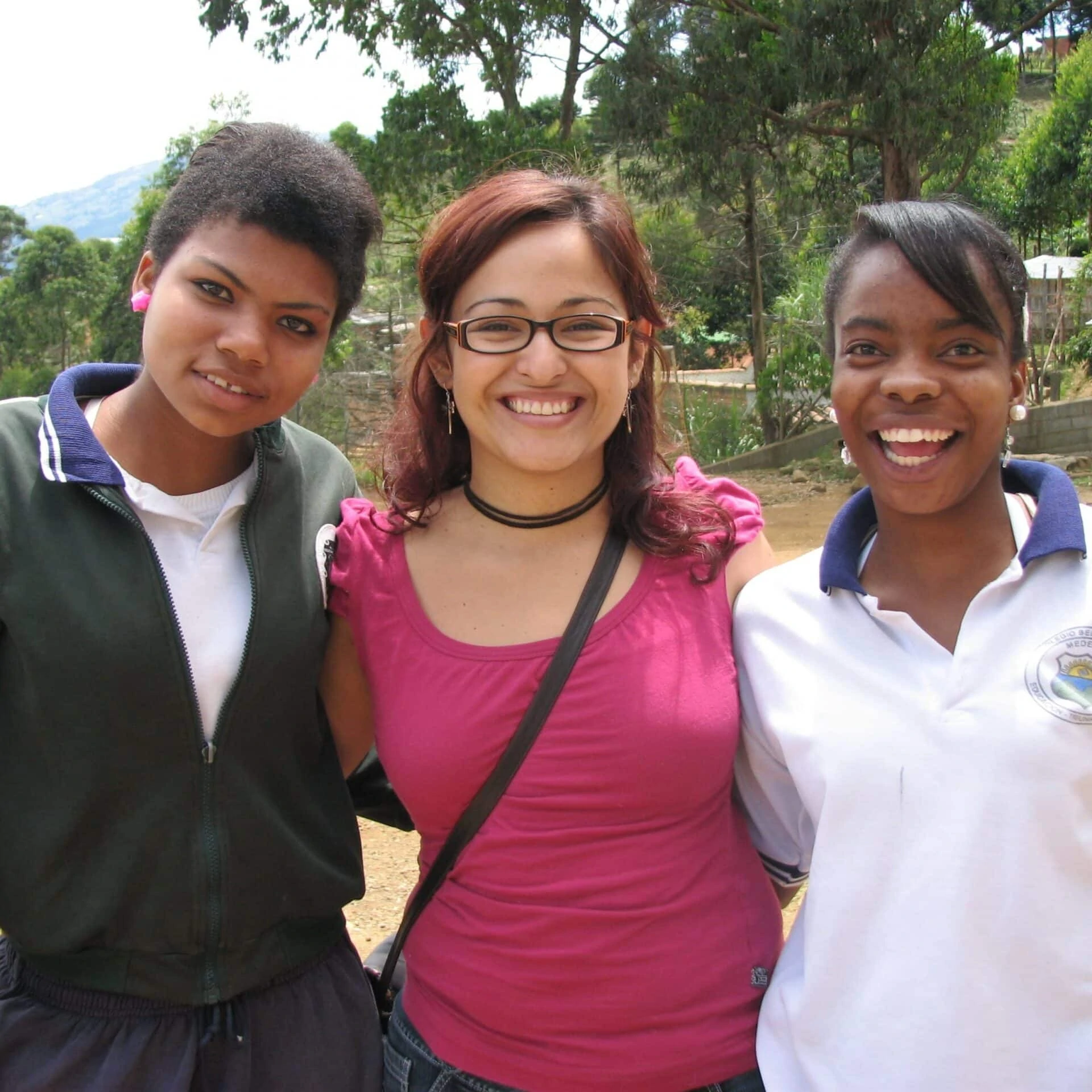 Three young women from Antioquia, Colombia stand smiling arm in arm.