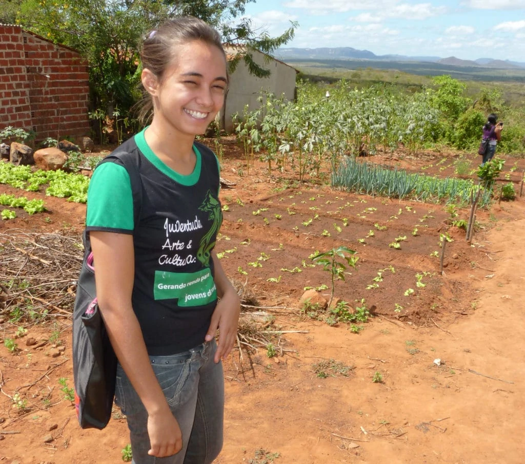 Eine junge Frau steht glücklich vor ihrem Gemüsegarten.