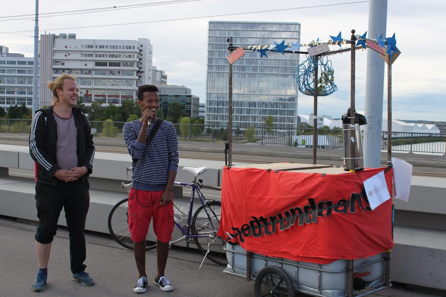 Black teenager on a city walk on the Dreirosenbrücke. Behind him is a bicycle with a wagon.