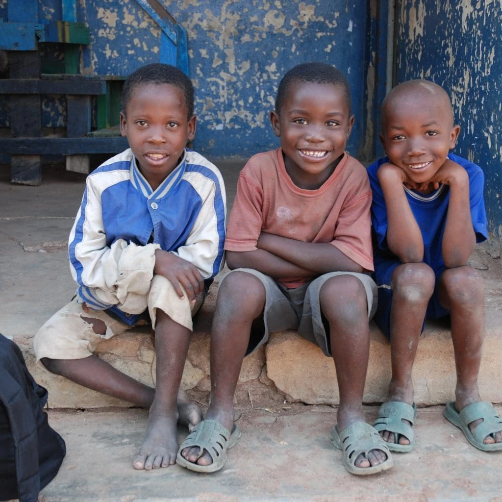 Drei schwarze Buben aus Tansania sitzen auf einer Türschwelle.