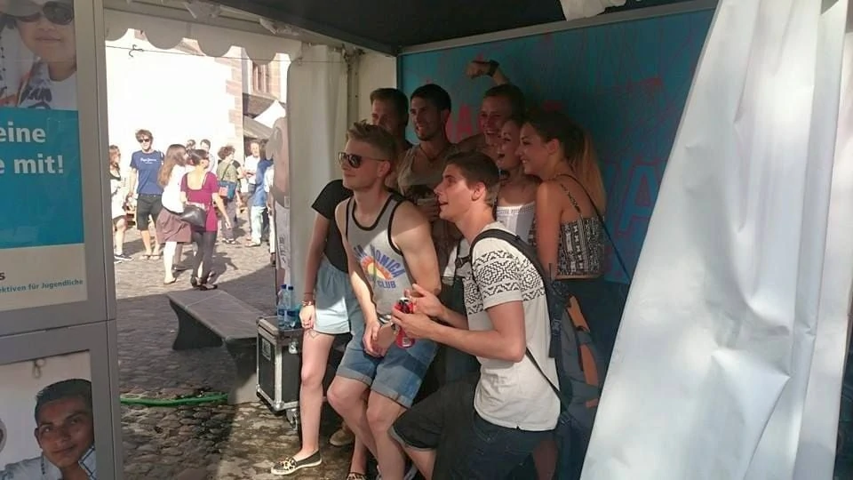 Young people stand in the tent in front of the photo box and have their picture taken together.