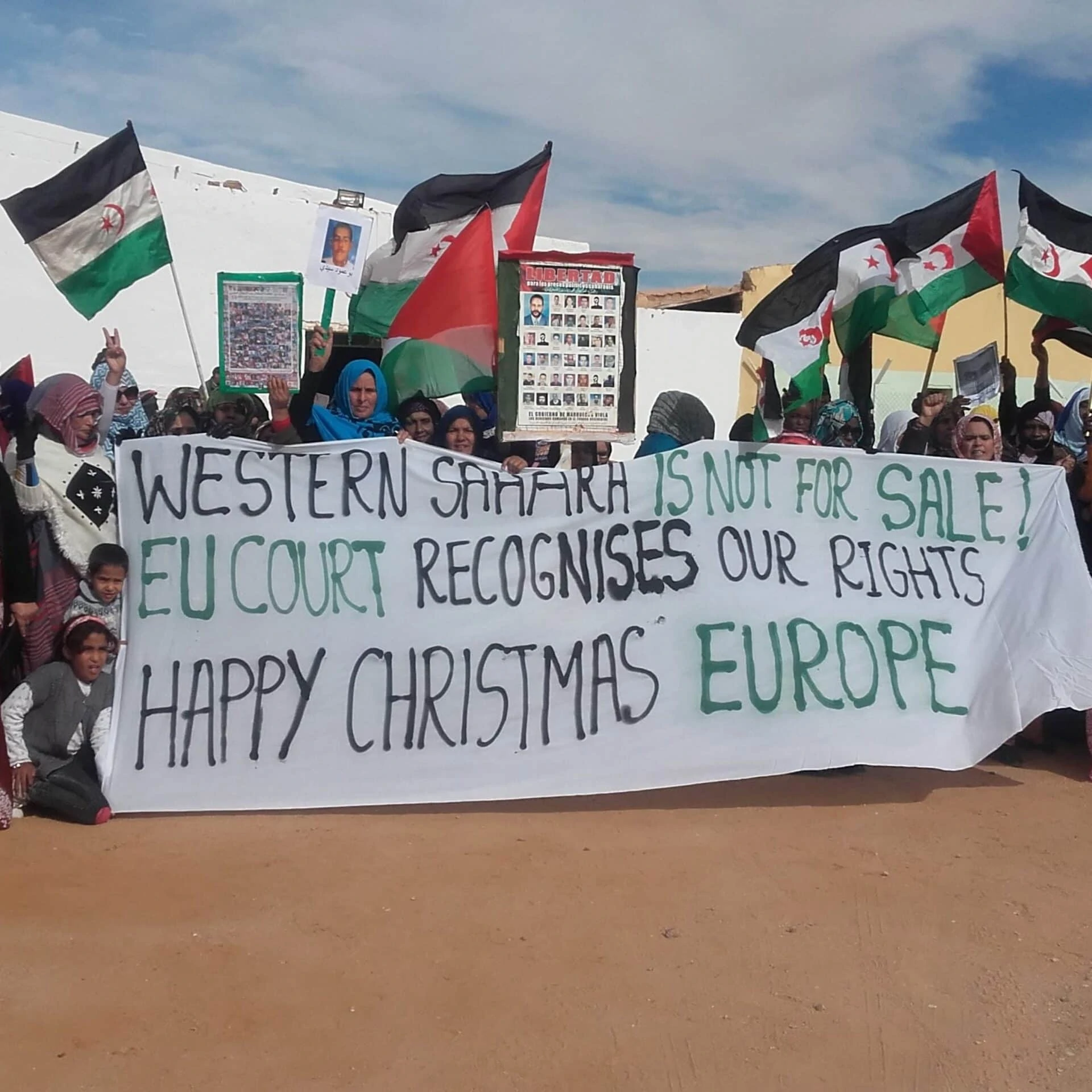 Es stehen eine Menge von Sahraouis in der Wüste im Halbkreis. Einige halten ein Transparent: Die Westsahara steht nicht zum Verkauf. Das EU-Gericht anerkennt unsere Rechte. Fröhliche Weihnachten Europa.