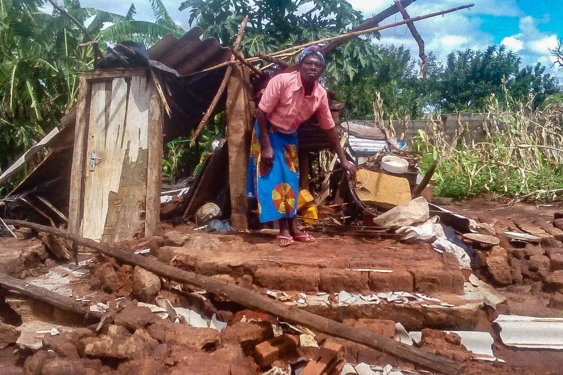 Black woman builds a temporary hut with pieces of corrugated iron.