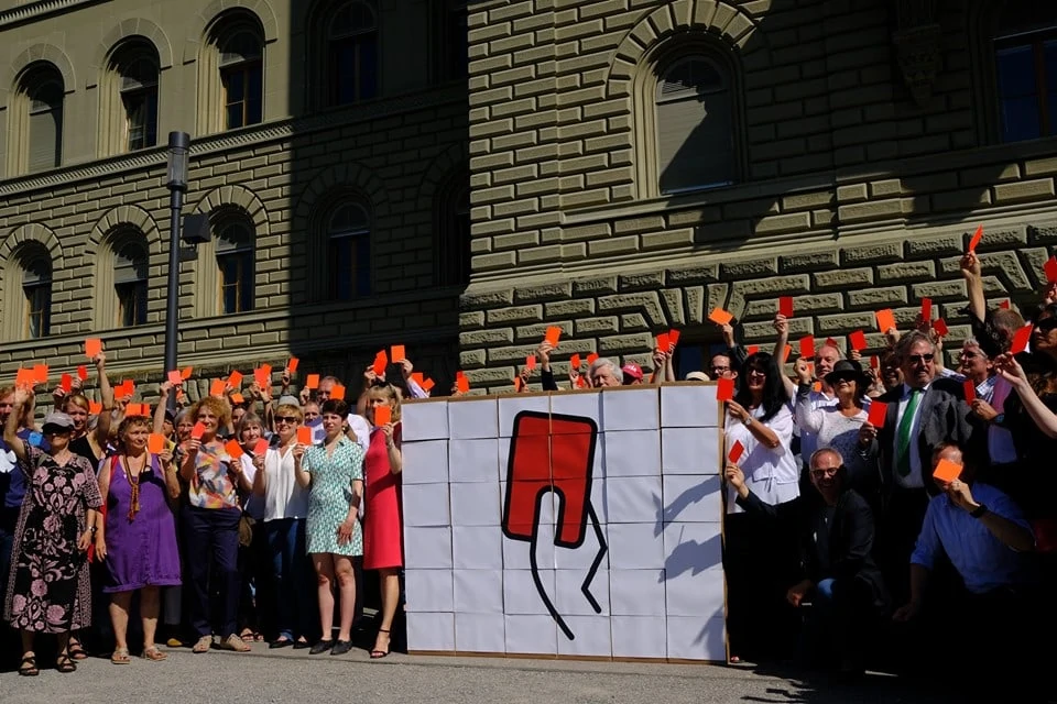 People in front of the Bundeshaus show red card.