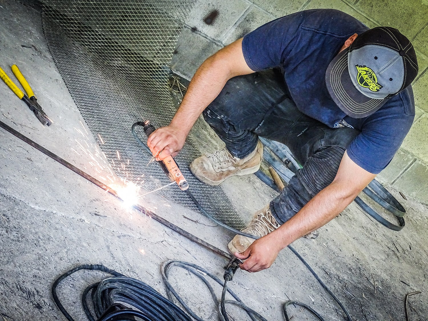 Ein junger Mann in der Hocke, ein Metallstück schweissend.