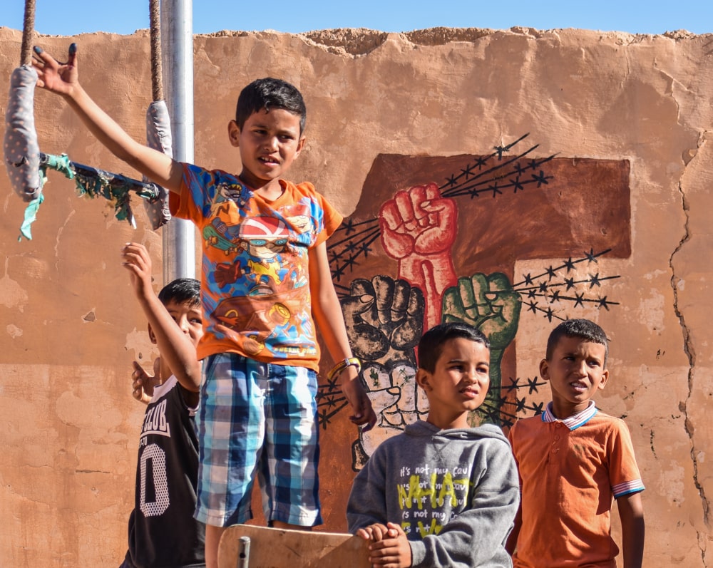Vier Jungs vor einer Lehmwand mit politischen Gafitti.