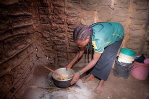 Aronia puts a pot on the small fireplace in her hut.