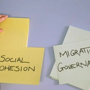 White wall with yellow and green pieces of paper on which is written "Social Cohesion" and "Migration Governance".