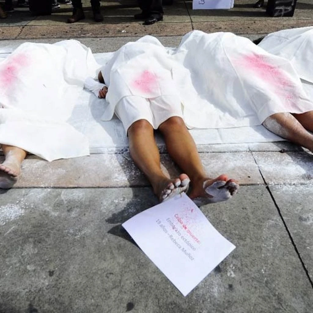 Women lie on the street under bloodstained white sheets.