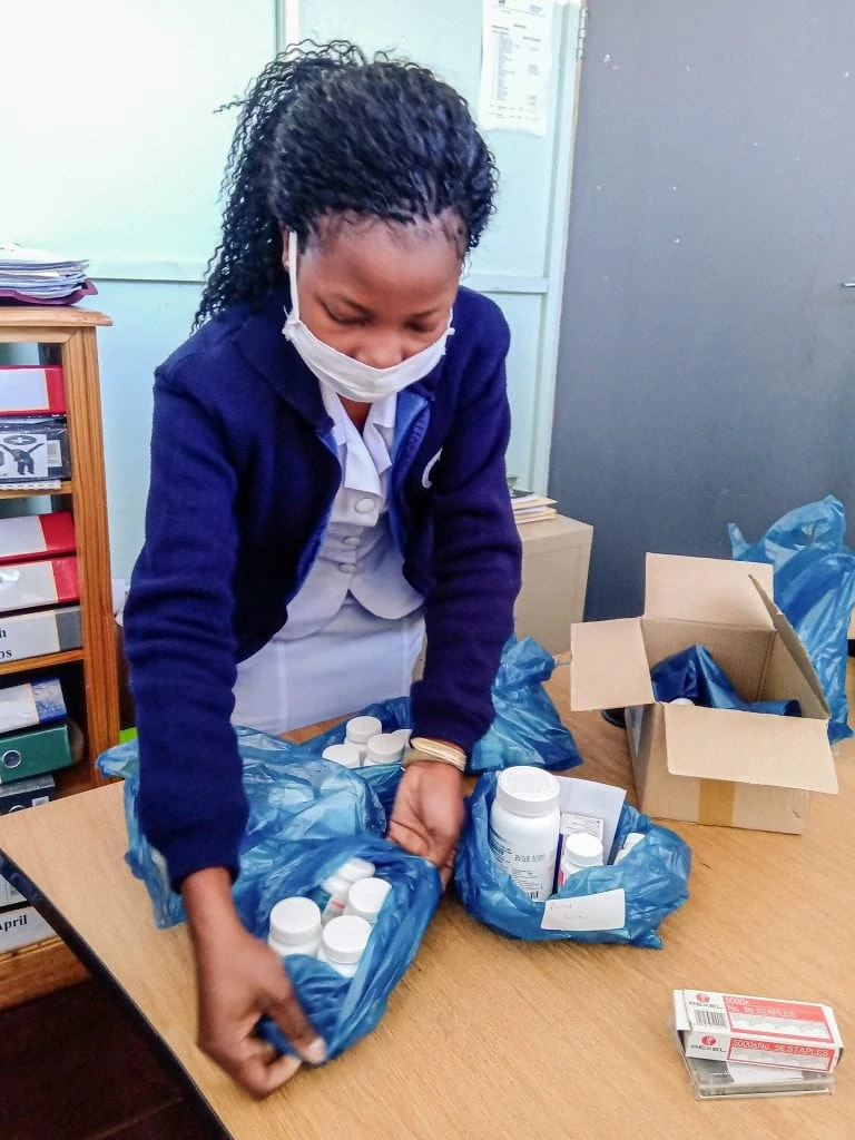 Schwarze Frau mit Mundschutz packt Medizin in blaue Plastikbeutel.