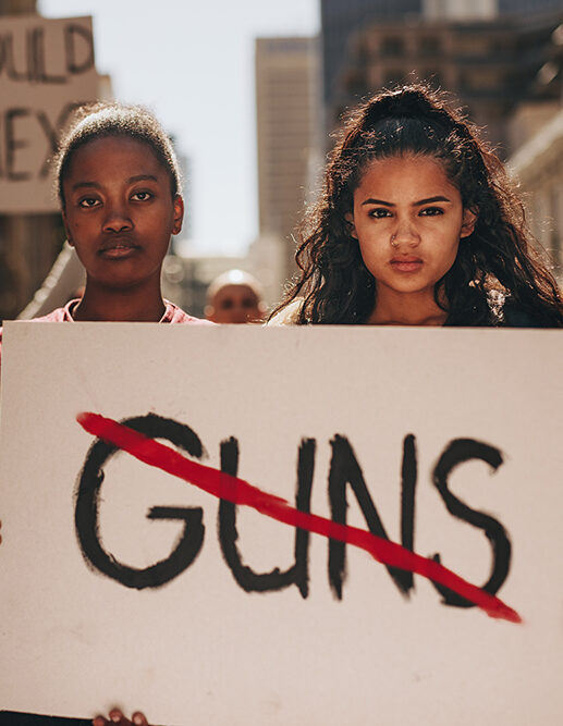 Girls hold sign "Guns" crossed out