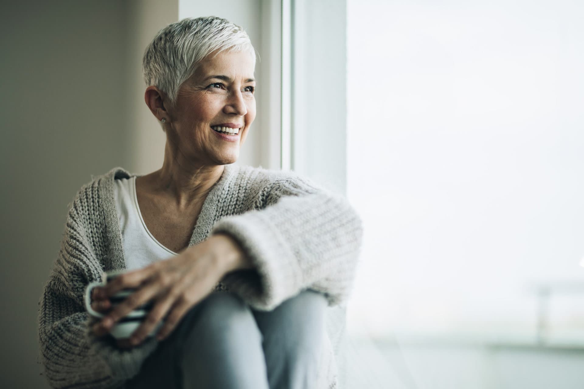 happy mature woman with coffee cup relaxing by the window.