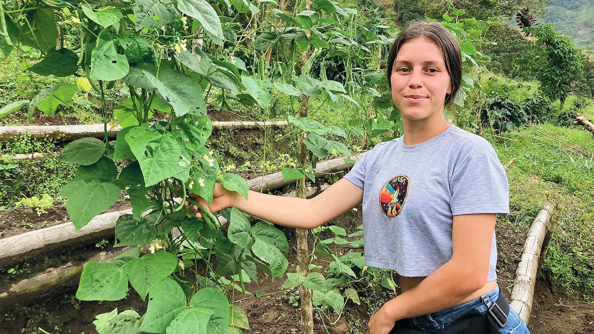 Eine-junge-Frau-auf-einem-Feld-hält-eine-Pflanze-in-ihrer-Hand.