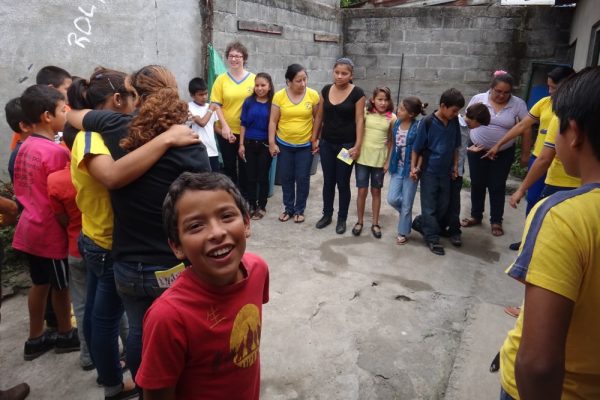 Kinder und Jugendliche stehen im Hinterhof eines Hause im Kreis und halten gegenseitig ihre Hände. Manche von ihnen haben blau-gelbe T-Shirts angezogen.