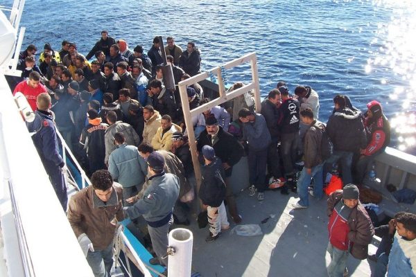 People from an overcrowded boat change to a larger naval vessel.