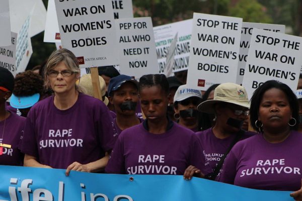 Women in purple T-shirts hold up white signs. In front of them a banner with the crawl Lifeline.