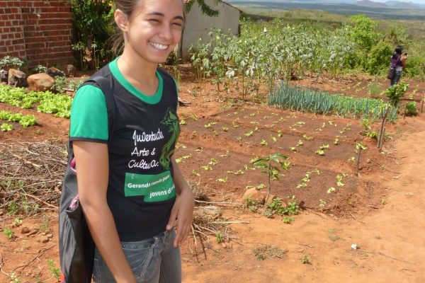 Eine junge Frau steht glücklich vor ihrem Gemüsegarten.