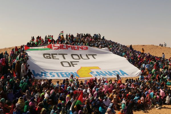 Many Sahrawis stand around a huge flag with the inscription: Siemens get out of Western Sahara.