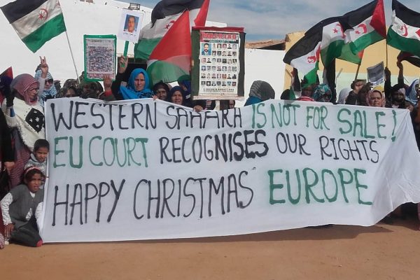 There are a lot of Sahraouis in the desert in a semicircle. Some hold a banner: Western Sahara is not for sale. The EU court recognises our rights. Merry Christmas Europe.
